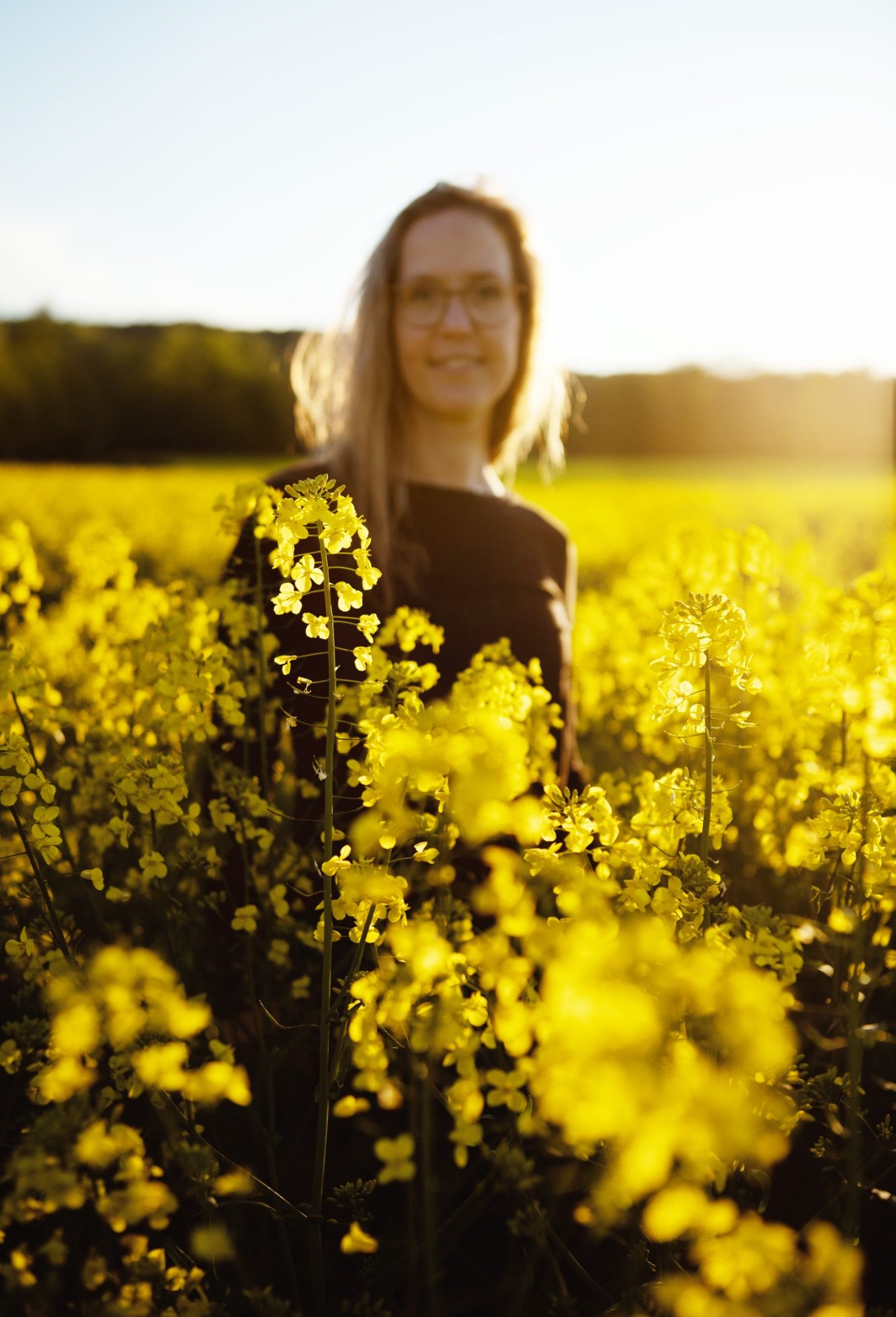 Frau mit Brille steht in einem blühenden Feld, umgeben von Raps.