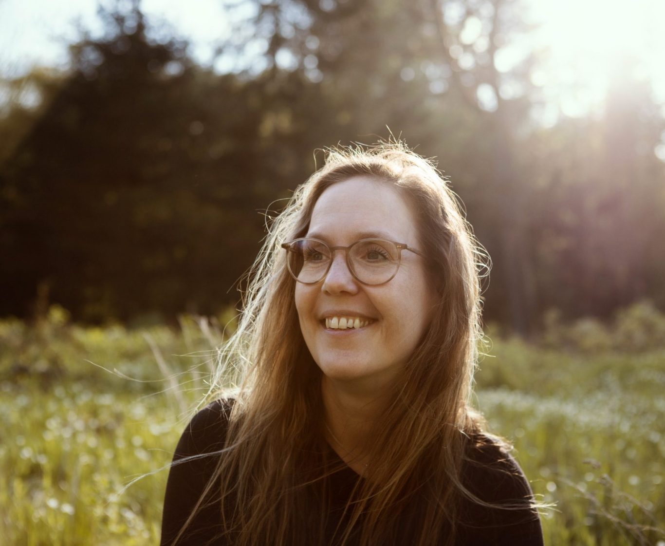 Frau mit Brille, die in einem sonnigen Wald mit Bäumen steht.