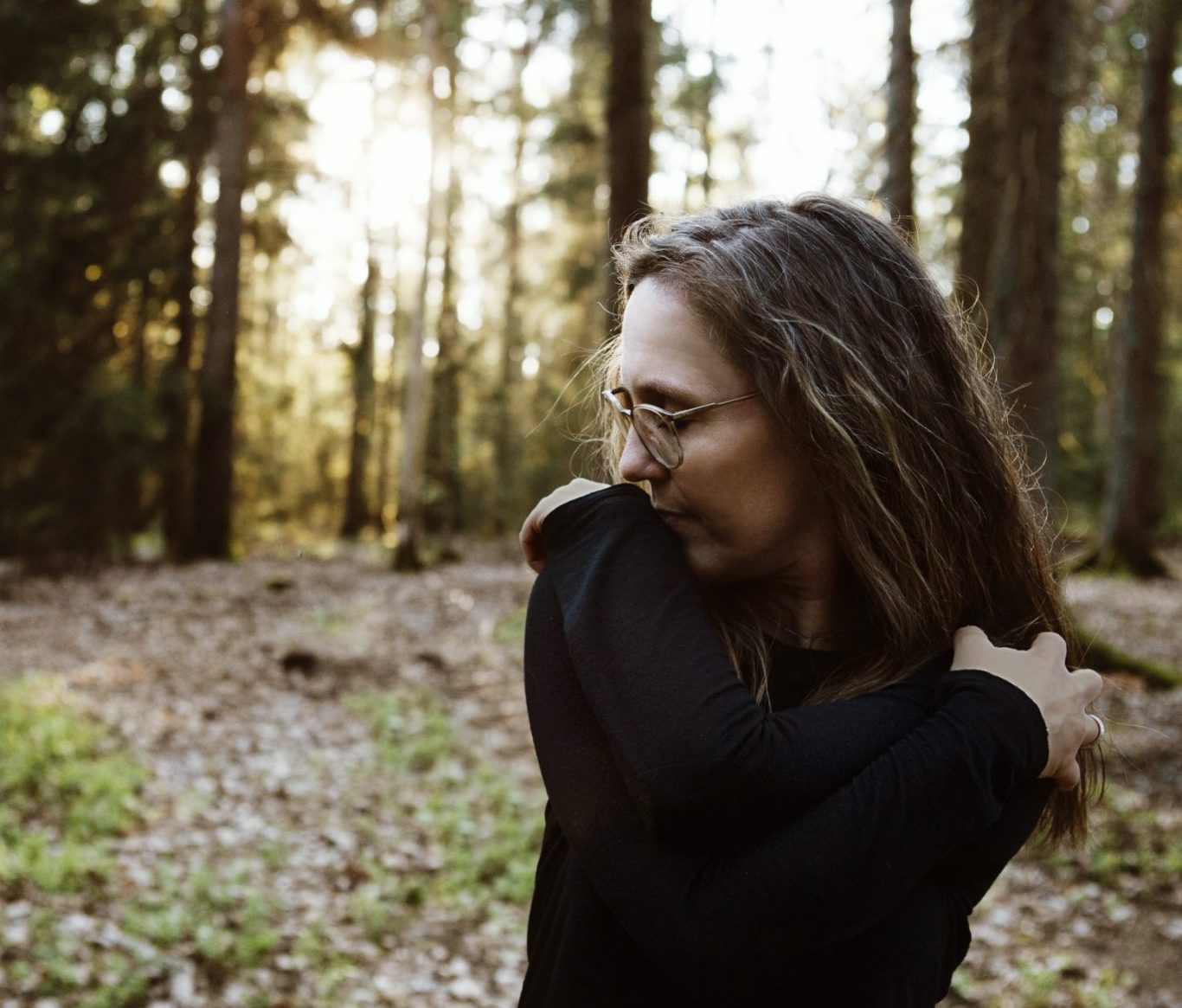 Frau mit Brille, die in einem sonnigen Wald mit Bäumen steht.