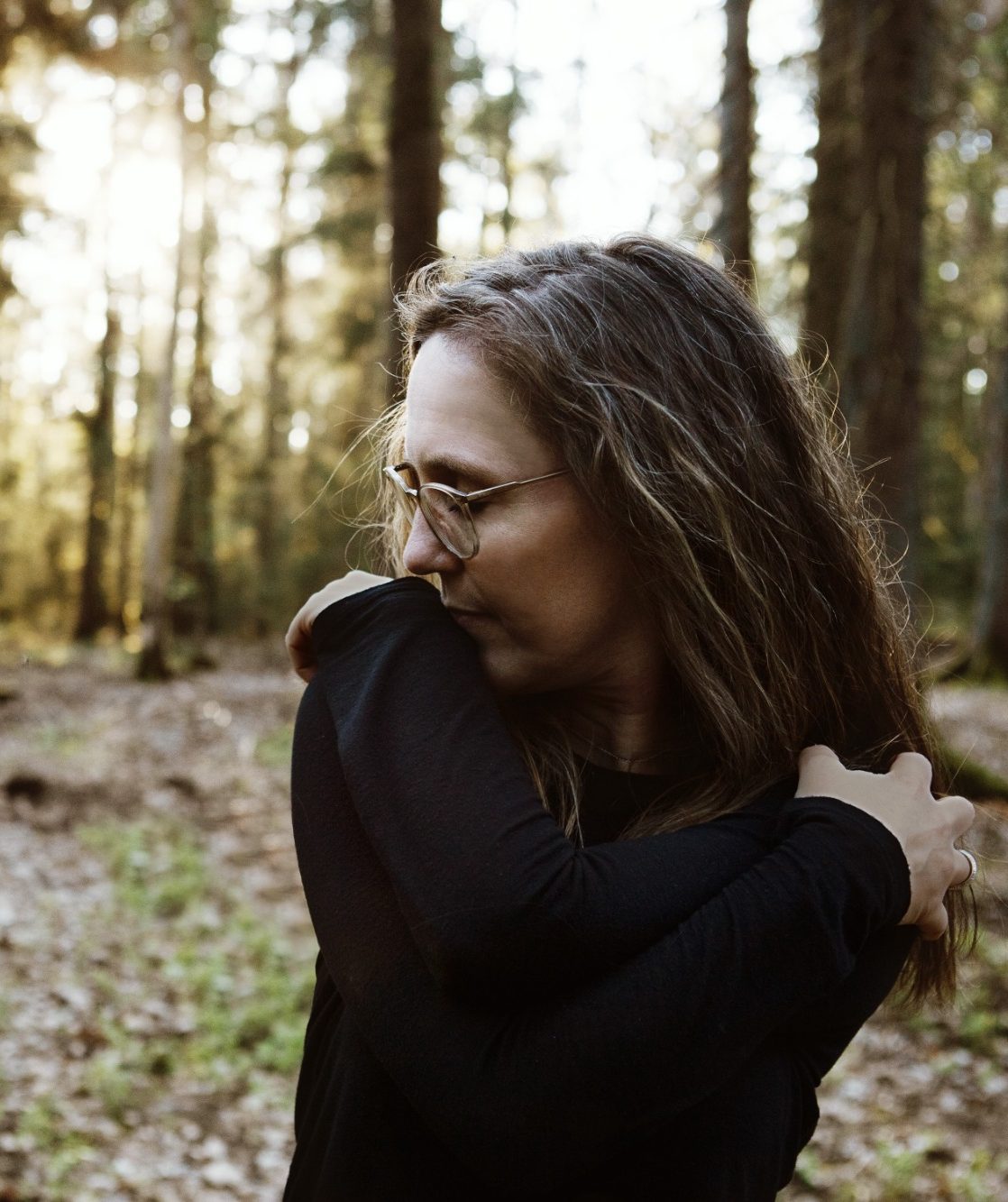 Frau mit Brille, die in einem sonnigen Wald mit Bäumen steht.
