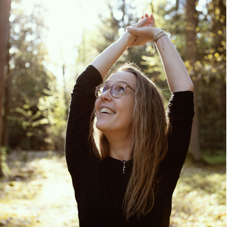 Frau mit Brille, die in einem sonnigen Wald mit Bäumen steht.